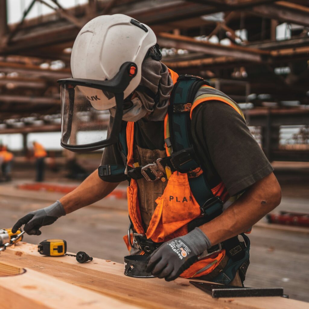 Construction worker in safety gear measuring lumber on a job site