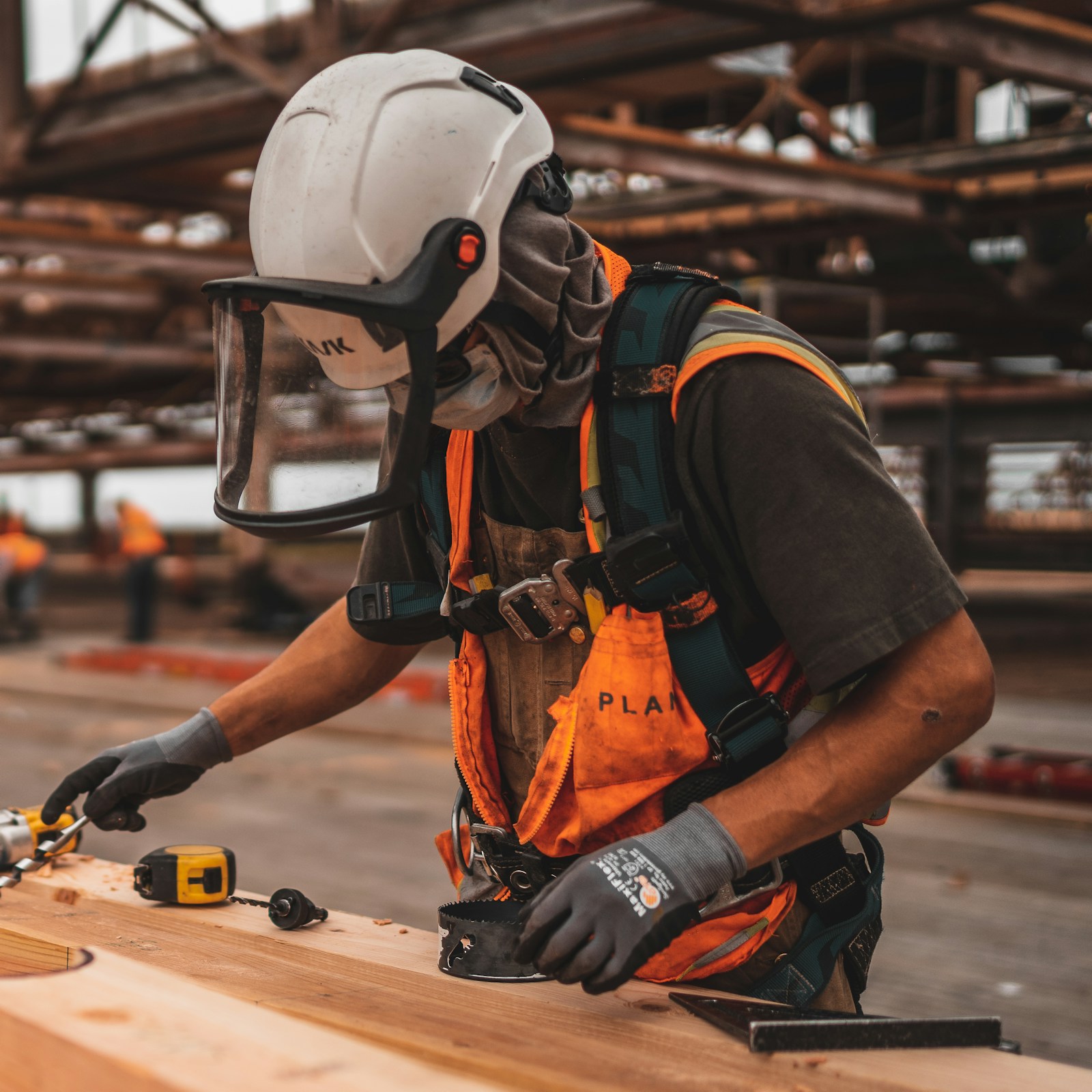 Construction worker in safety gear measuring lumber on a job site