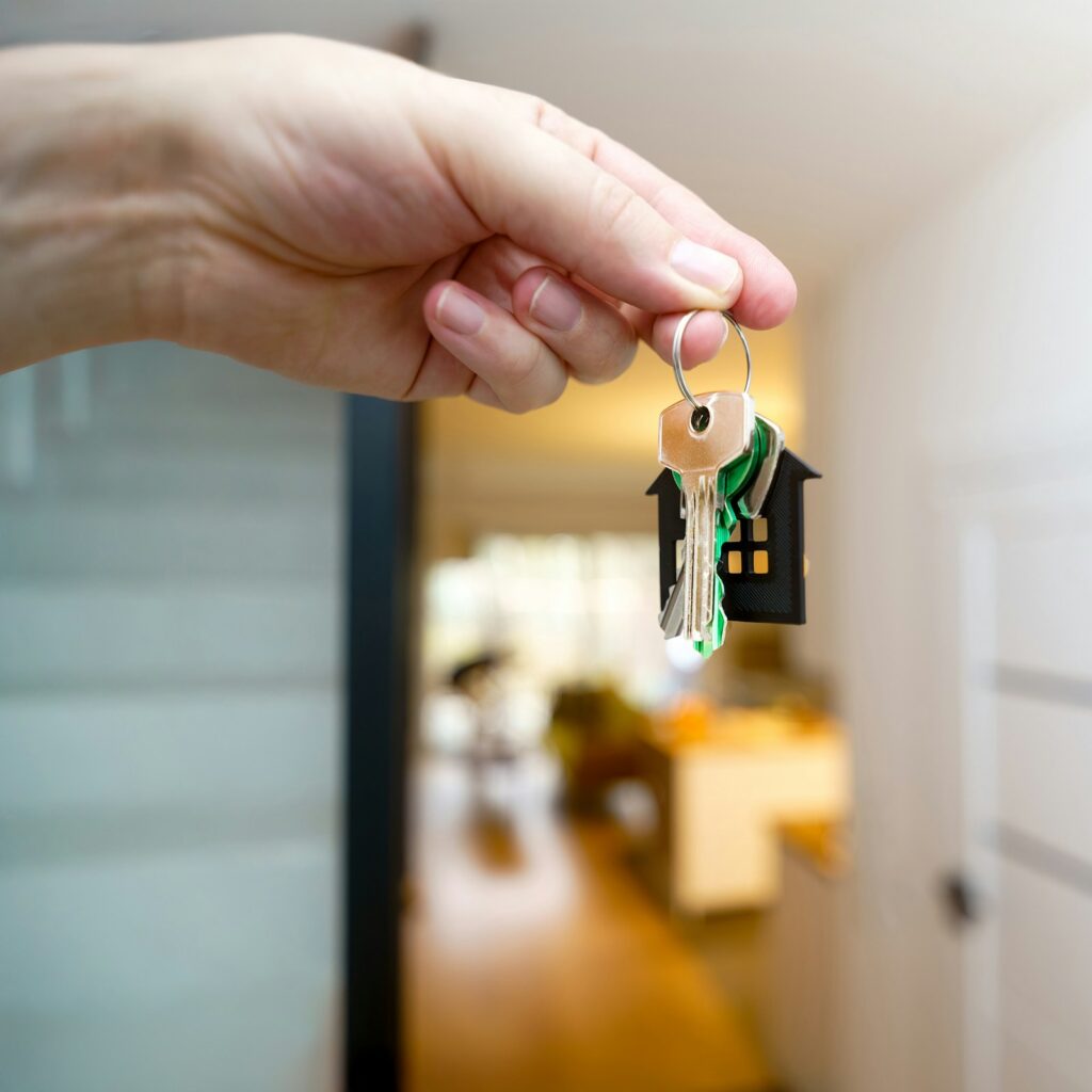 Hand holding house keys in front of a home entrance