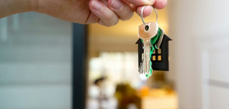 Hand holding house keys in front of a home entrance