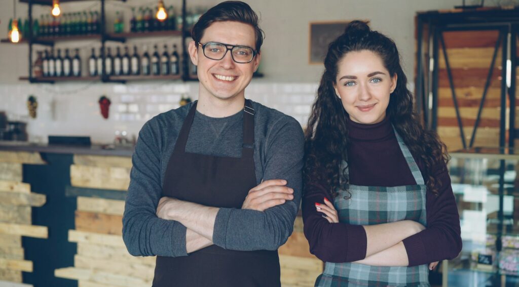 Two cafe owners standing proudly inside their coffee shop
