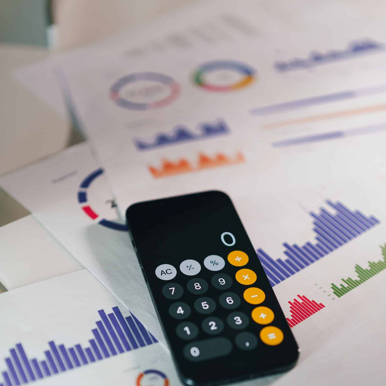 Calculator resting on printed financial reports and charts