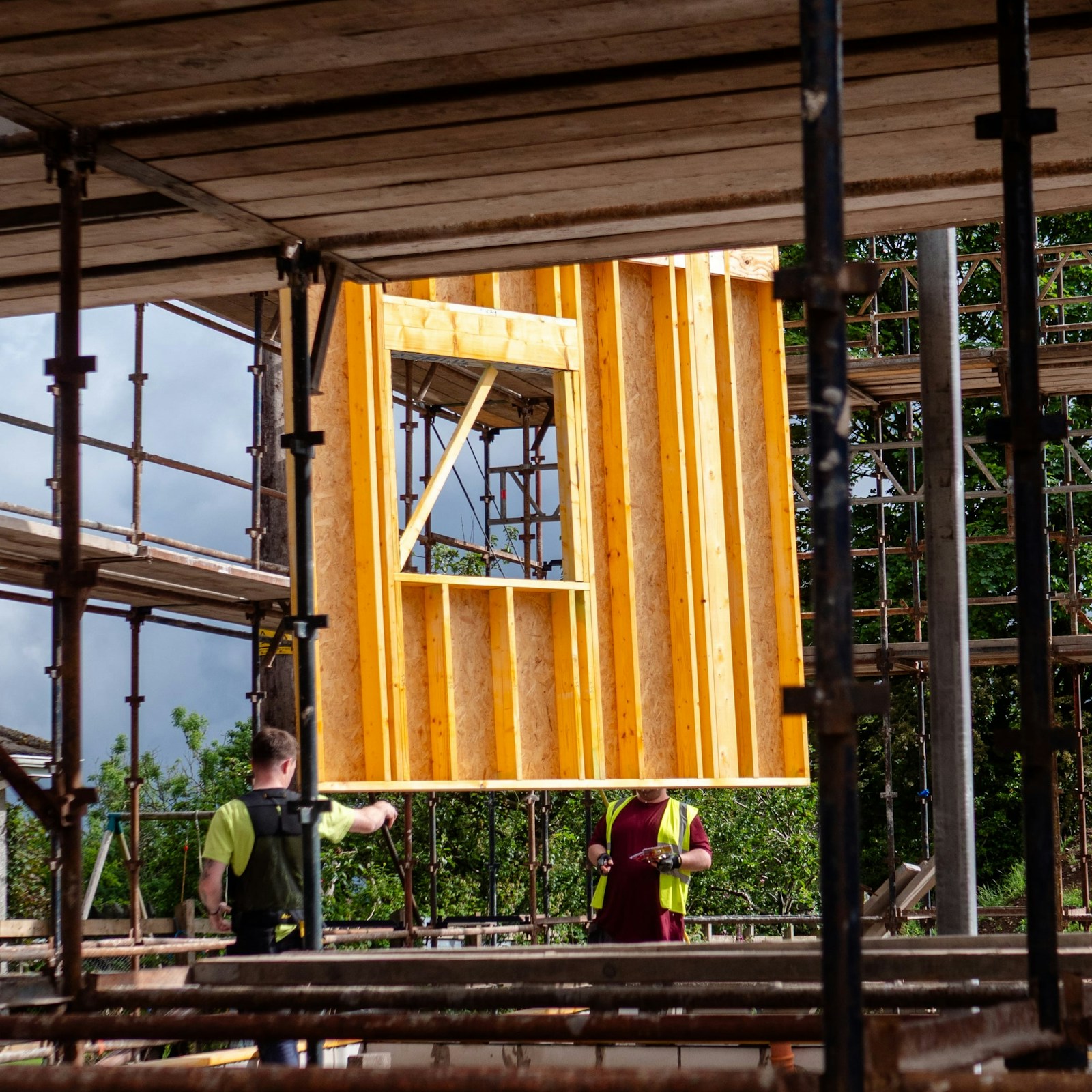 Two construction workers lifting a framed wall into place on a building site